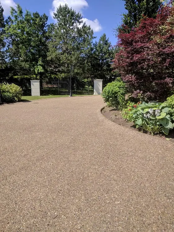 Wide aggregate driveway surrounded by mature garden planting