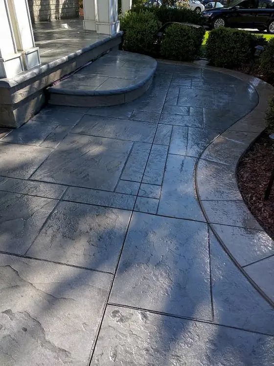 Grey stamped concrete walkway curving beside a garden bed
