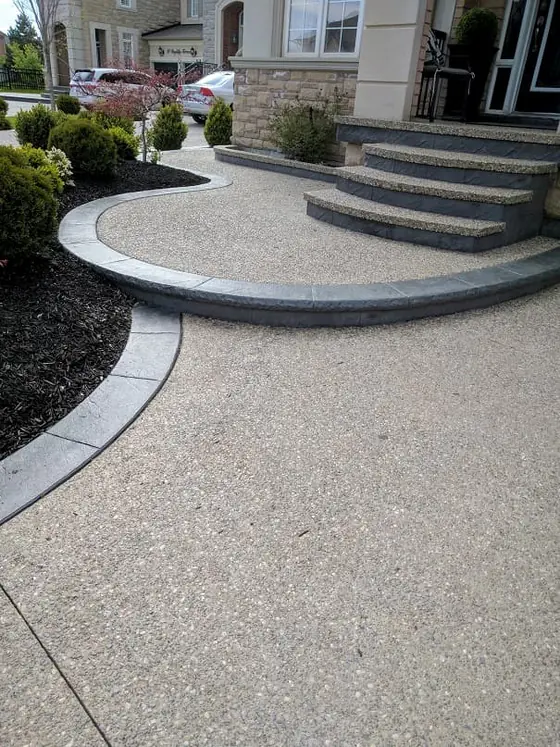 Curved exposed aggregate walkway beside a garden and front steps