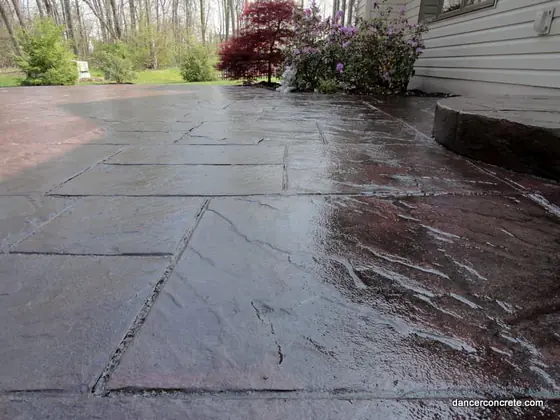 Dark finished stamped concrete patio beside landscaped garden beds