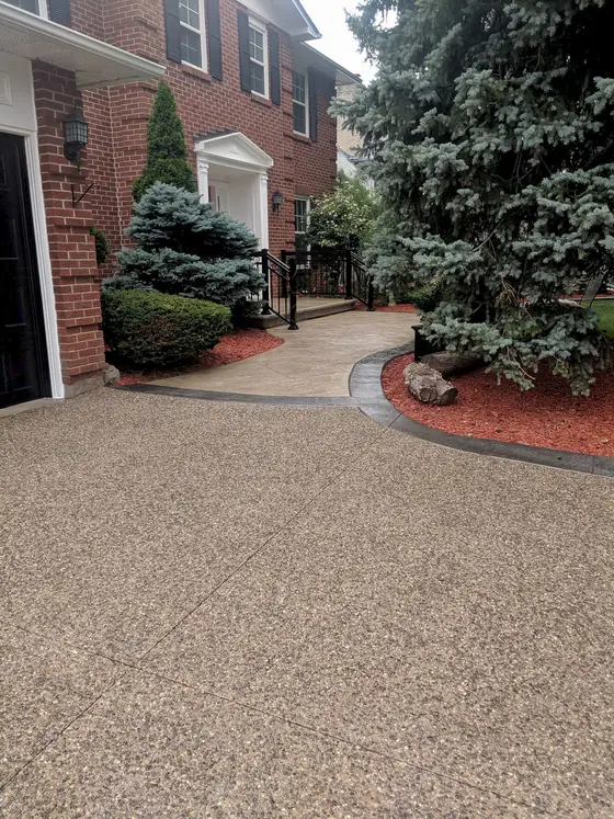 Exposed aggregate driveway and curved stamped walkway beside evergreens and a brick home